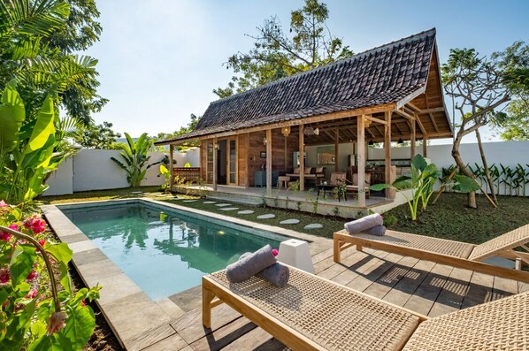 A poolside area with lounge chairs, a covered seating area, and a pool. - Villa We We - 1 Br (Pecatu)