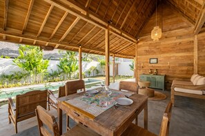 A wooden dining area with a table set for two, surrounded by chairs, a bench, and a sofa. - Villa We We - 1 Br (Pecatu)