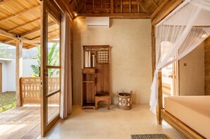 A room with a wooden bed, a wooden cabinet, a small stool, and a woven basket. - Villa We We - 1 Br (Pecatu)