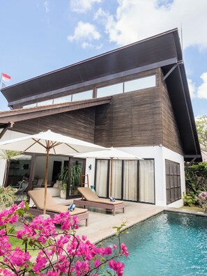 Ein modernes Haus mit Schwimmbad, Liegestühlen und einem großen Sonnenschirm.