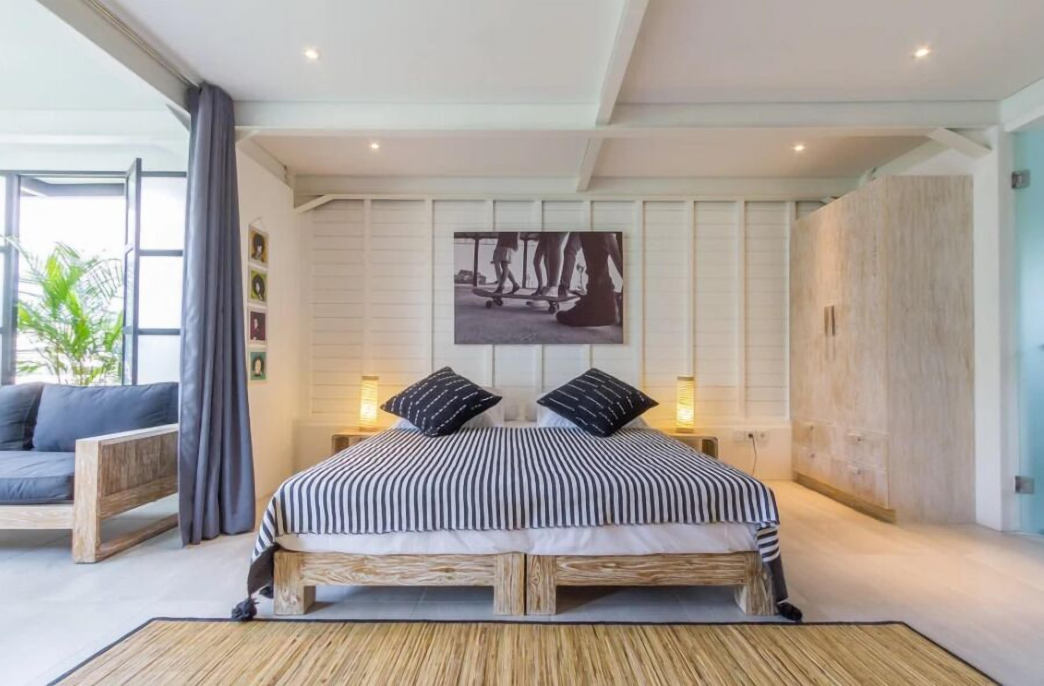 A bedroom with a bed, a sofa, a large window, and a wall-mounted picture.
