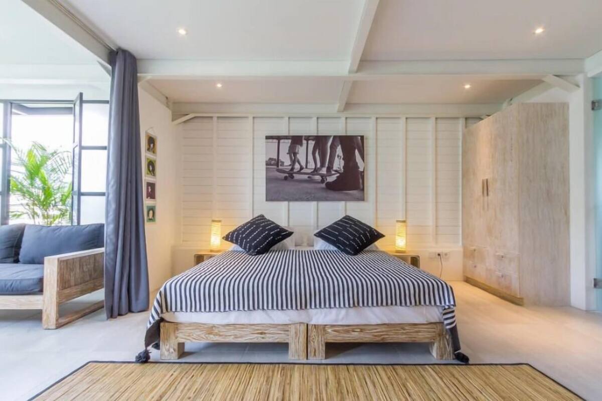 A bedroom with a bed, a sofa, a large window, and a wall-mounted picture.