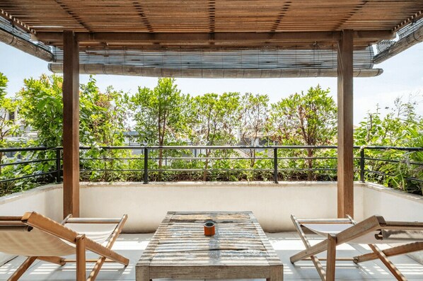 A covered outdoor seating area with a table and chairs, surrounded by greenery and a metal railing. - Batubolong - Studio (Canggu)