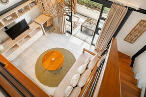A modern living room with a flat-screen TV, a round coffee table, a sofa, and a dining area with a table and chairs. - Batubolong - Studio (Canggu)