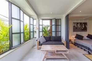 A spacious living area with a sofa, a coffee table, and a bed with striped bedding. - Batubolong - Studio (Canggu)