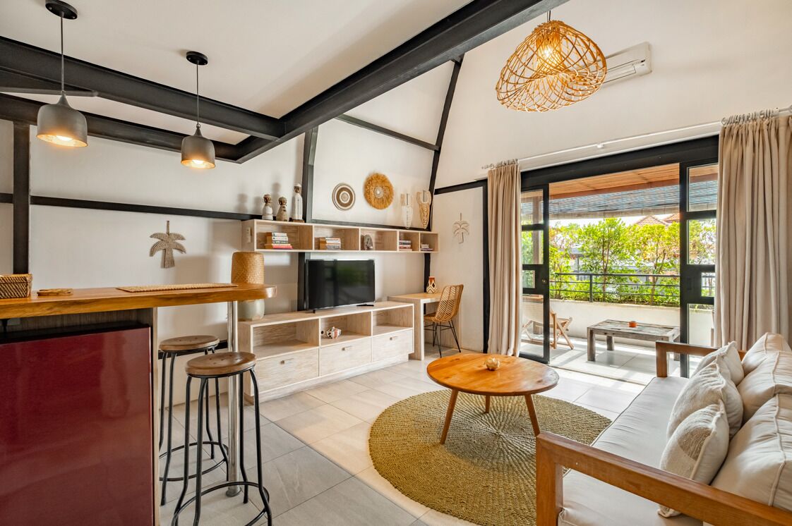 A modern living room with a sofa, a coffee table, a TV, and a dining area with a bar.