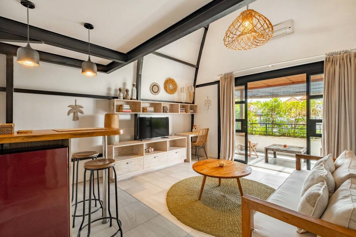 A modern living room with a sofa, a coffee table, a TV, and a dining area with a bar.