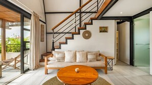 Un salon moderne avec un canapé, une table basse, un escalier et une vue à travers une porte vitrée.