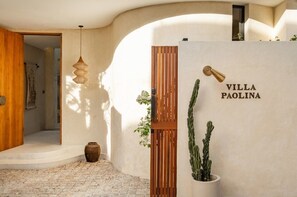 Ein Empfangsbereich mit Holztür, einer Pendelleuchte, einem Blumentopf und einem Schild mit der Aufschrift 'VILLA PAOLINA'.