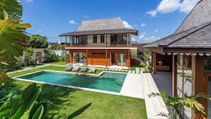 Una casa de dos pisos con piscina, balcón y jardín.