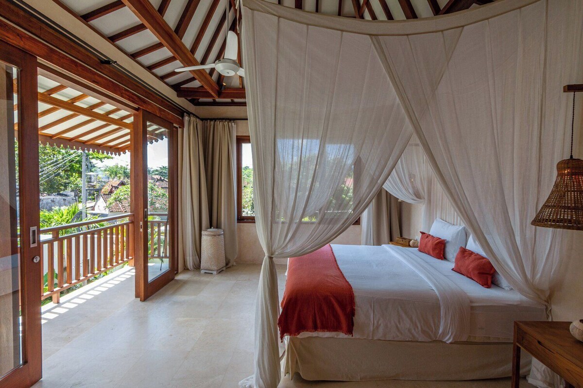 A room with a bed, a ceiling fan, and a view of the outdoors.