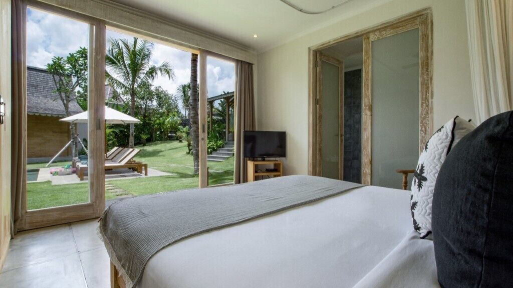Ein Schlafzimmer mit einem großen Bett, einem Fernseher und Blick auf einen Garten mit Palmen.