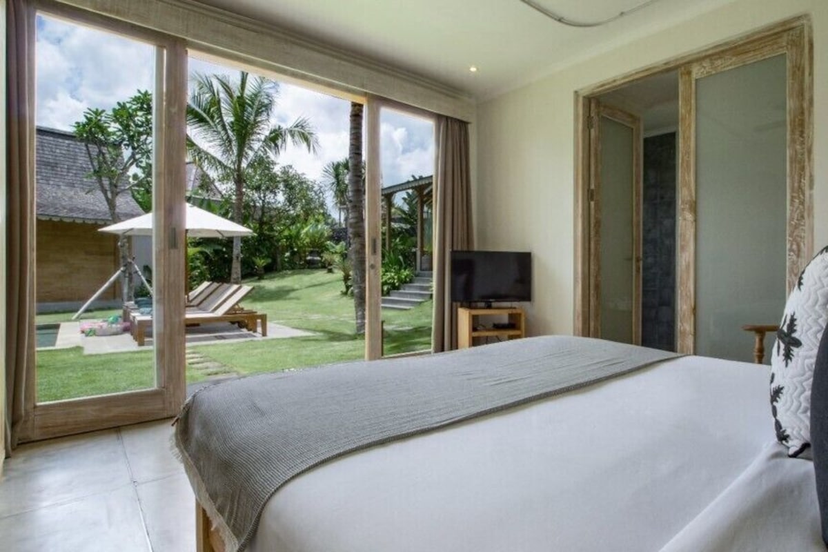 A bedroom with a large bed, a television, and a view of a garden with palm trees.