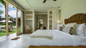 Un dormitorio espacioso con una cama grande, cabecero de madera y vistas a un jardín exuberante a través de amplias puertas correderas.