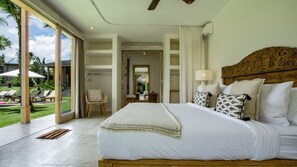 Ein geräumiges Schlafzimmer mit einem großen Bett, einem Holzkopfstück und Blick auf einen üppigen Garten durch große Schiebetüren.