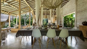 Un comedor con una mesa larga, cuatro sillas, techo de vigas de madera y lámparas colgantes.