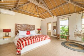 Ein Schlafzimmer mit Bett, Nachttischen, einem Hängekorbstuhl, einer Bank und einem großen Fenster mit Blick auf Grünflächen.