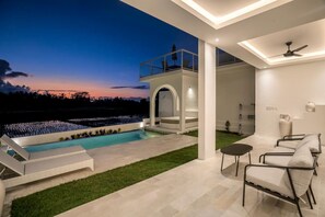 A modern outdoor pool area with a view of the sunset, a covered seating area, and a patio with chairs and a table. - Villa Chai - 2 Br (Ubud)