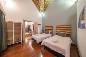 Ein Hotelzimmer mit zwei Betten, Holzboden, einer Deckenleuchte und einem Bild an der Wand.