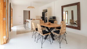 Un comedor moderno con una mesa de madera y sillas de mimbre, una cocina al fondo y un espejo grande en la pared.