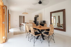 Ein moderner Essbereich mit einem Holztisch und Korbstühlen, eine Küche im Hintergrund und ein großer Spiegel an der Wand.