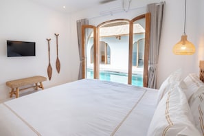 Ein Schlafzimmer mit einem großen Bett, einem Fernseher, Holzschlägern, einer Bank und Blick auf einen Pool.