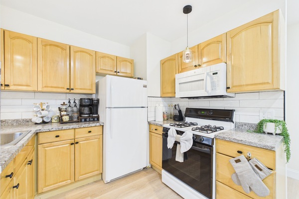 Bright full kitchen with gas stove, coffee station, and warm wood cabinets