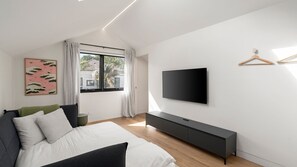A modern bedroom with a bed, a TV, a console table, and a window with curtains. - Loft & Leaf Terrace Stanmore (Stanmore)