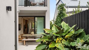 A modern house with a balcony, a dining area with a table and chairs, and a large plant in the foreground. - Loft & Leaf Terrace Stanmore (Stanmore)