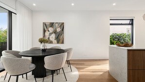 A modern dining area with a round table, six chairs, a vase with flowers, and a painting on the wall. - Loft & Leaf Terrace Stanmore (Stanmore)