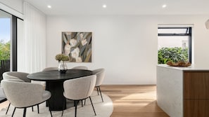 A modern dining area with a round table, six chairs, a vase with flowers, and a painting on the wall. - Loft & Leaf Terrace Stanmore (Stanmore)