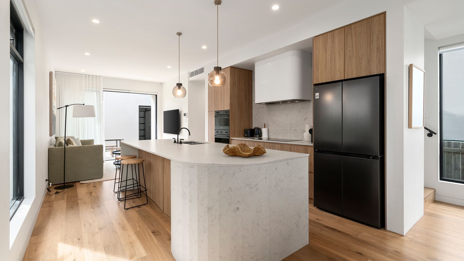 Een moderne keuken met een centraal eiland, houten keukenkastjes, een zwarte koelkast en een zithoek met een bank en barkrukken.