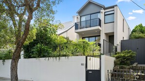 A modern two-story house with a balcony, a white wall with a gate, and lush greenery. - Loft & Leaf Terrace Stanmore (Stanmore)