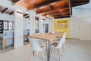 Un comedor con mesa y sillas de madera, un armario amarillo y un techo alto con vigas a la vista.