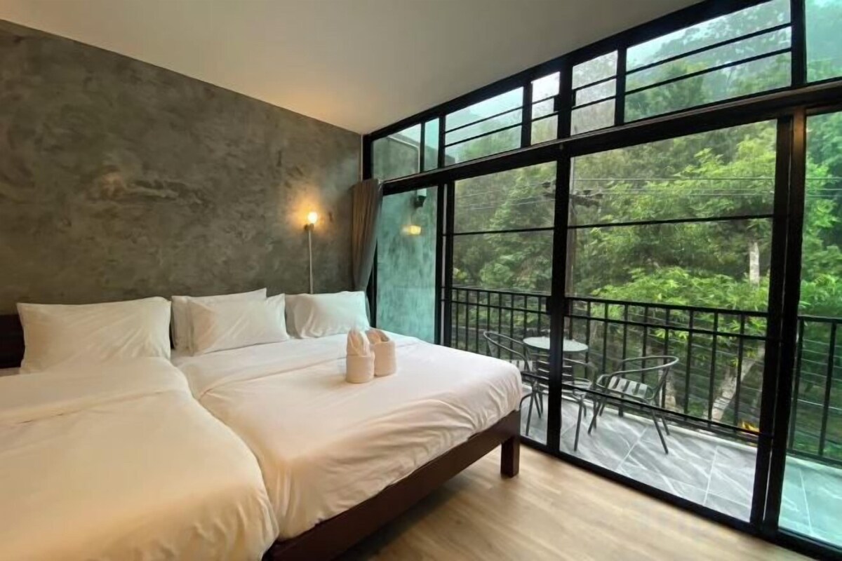 Un dormitorio con una cama grande, una mesita de noche y una ventana con vistas a la vegetación.