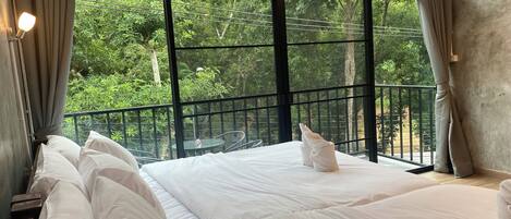 Habitación de hotel con un ventanal grande, una cama con ropa blanca y vistas a zonas verdes.