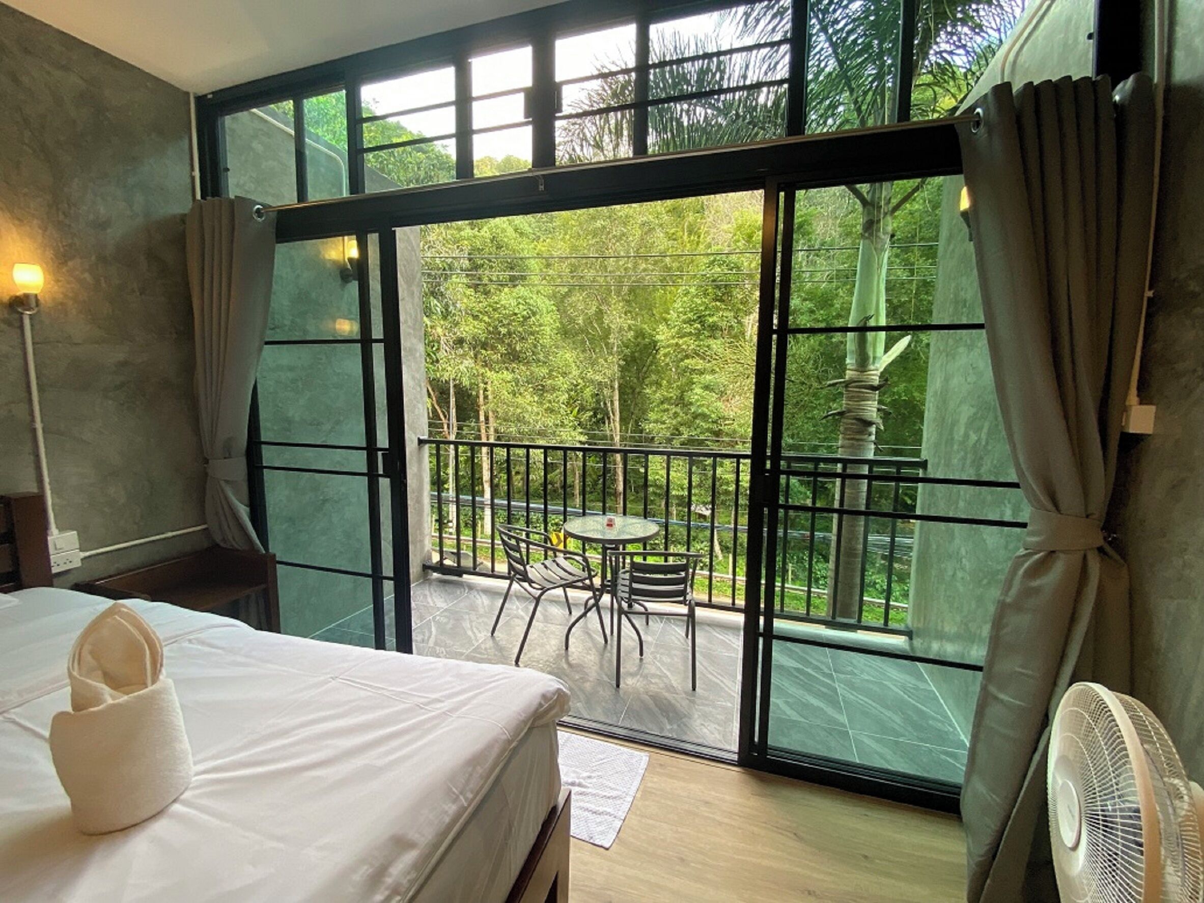A room with a bed, a fan, and a balcony with a table and chairs.