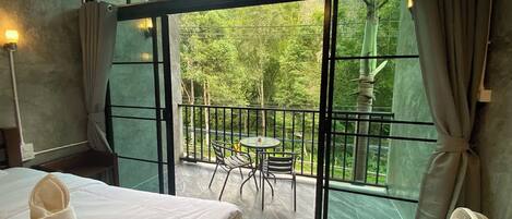 A room with a bed, a fan, and a balcony with a table and chairs.