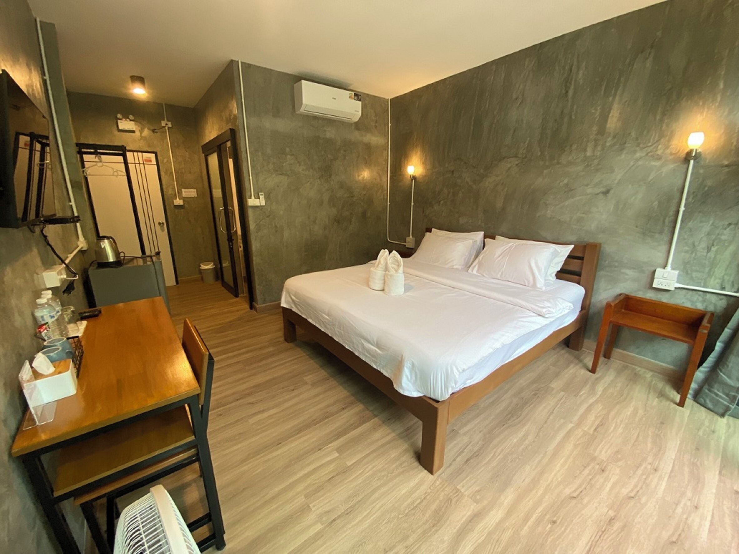 Habitación de hotel con cama, mesitas de noche, escritorio, silla, ventilador y aire acondicionado.