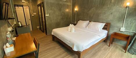 Habitación de hotel con cama, mesitas de noche, escritorio, silla, ventilador y aire acondicionado.