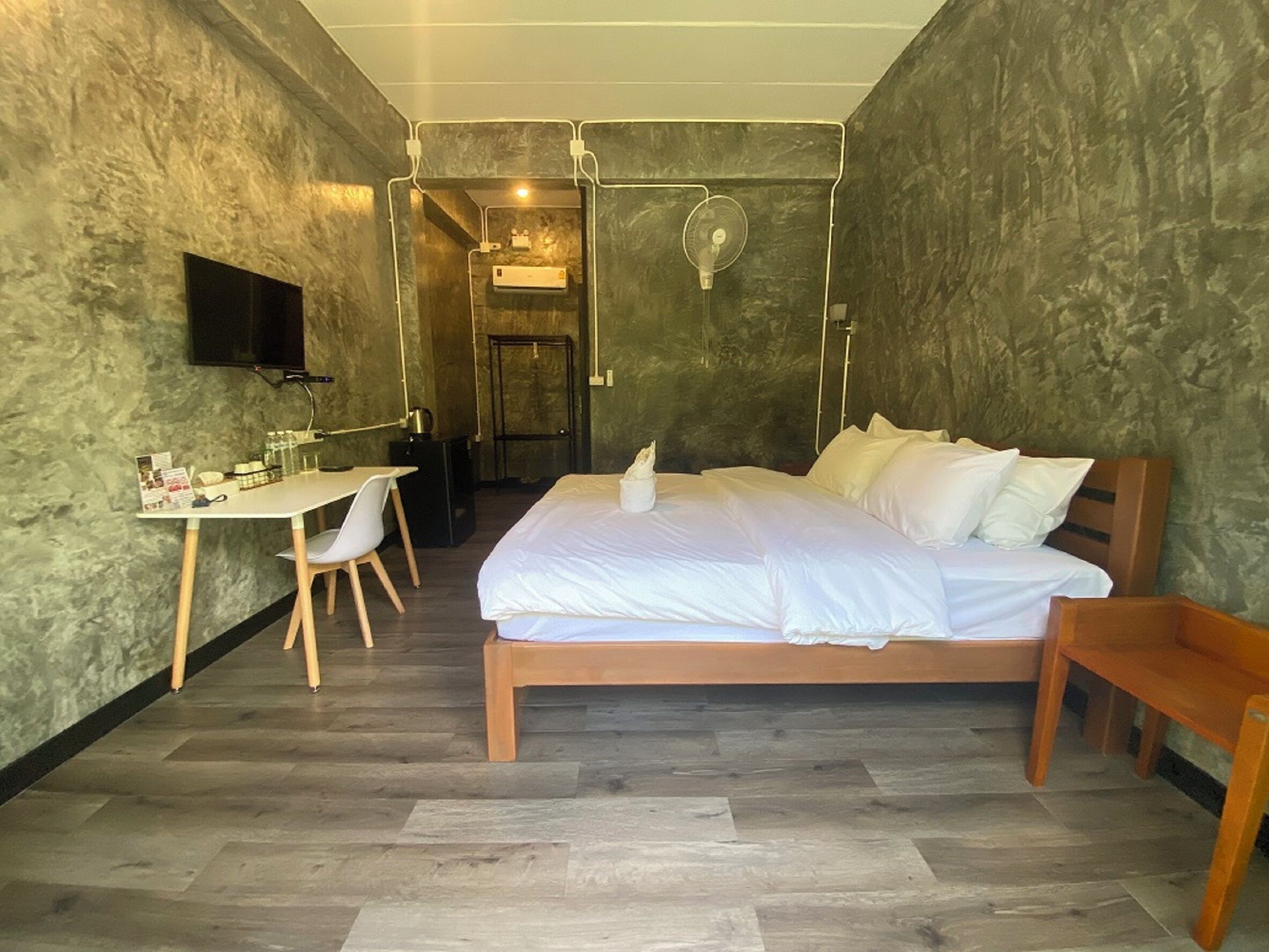 Un dormitorio con cama, escritorio, silla, televisor y baño visible a través de una puerta abierta.