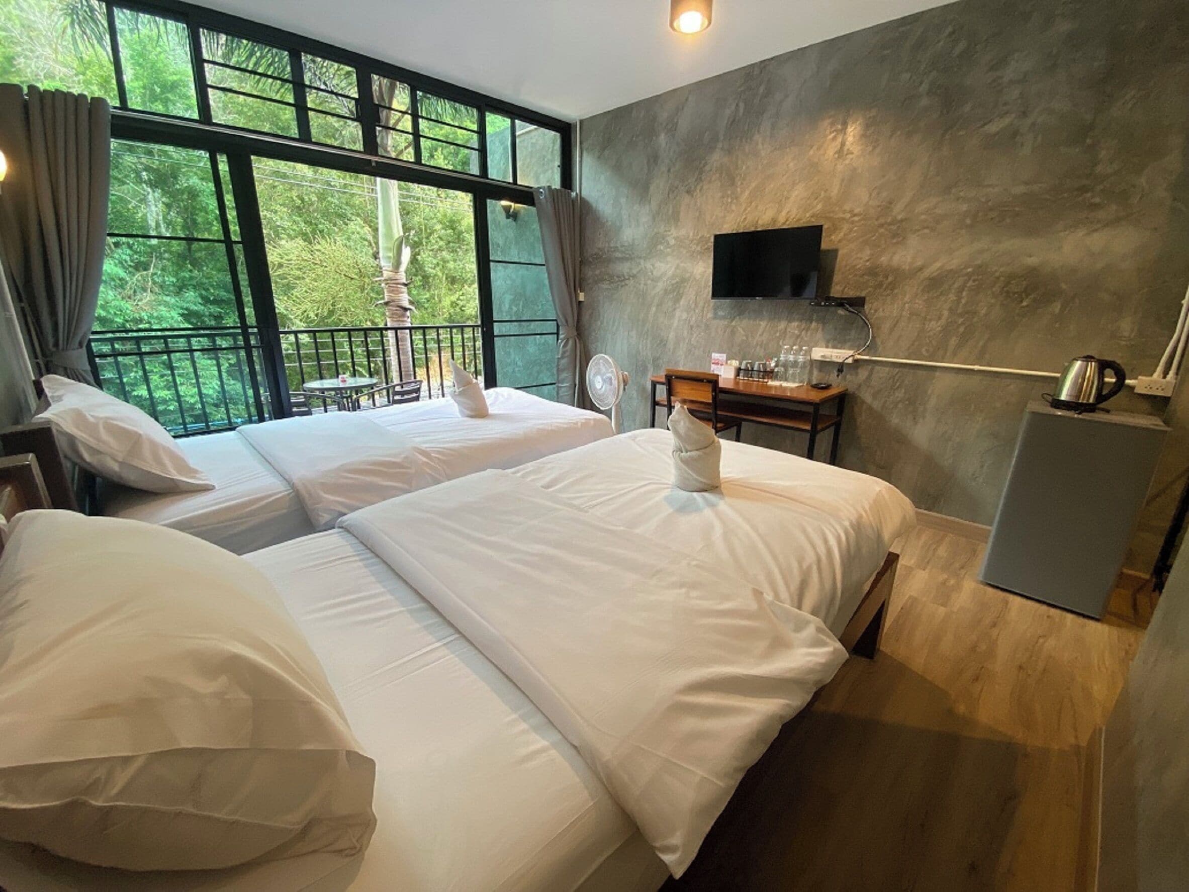 Habitación de hotel con dos camas, televisión, escritorio con silla y vistas a zonas verdes a través de amplios ventanales.