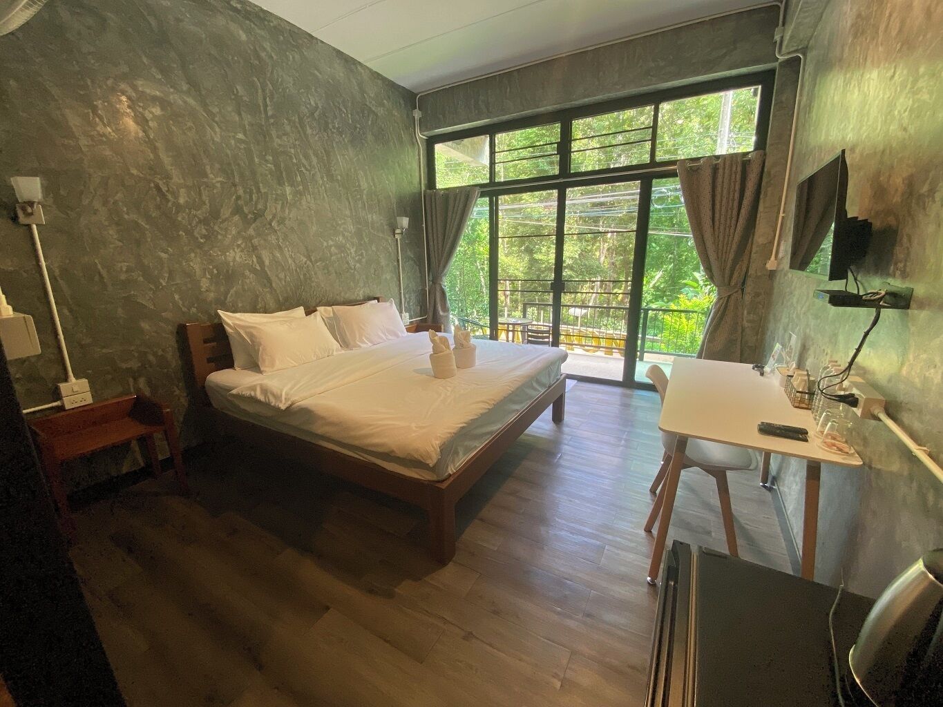 A bedroom with a wooden bed, a small desk, a chair, and a large window with curtains.