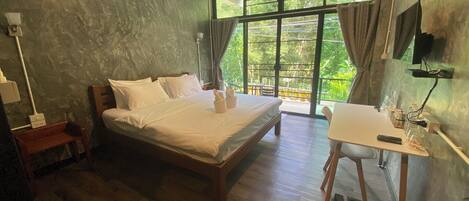 A bedroom with a wooden bed, a small desk, a chair, and a large window with curtains.