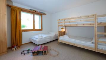Une chambre avec deux lits superposés, une fenêtre avec des rideaux, une petite table de chevet avec une lampe et une maison de jeu posée sur le sol.