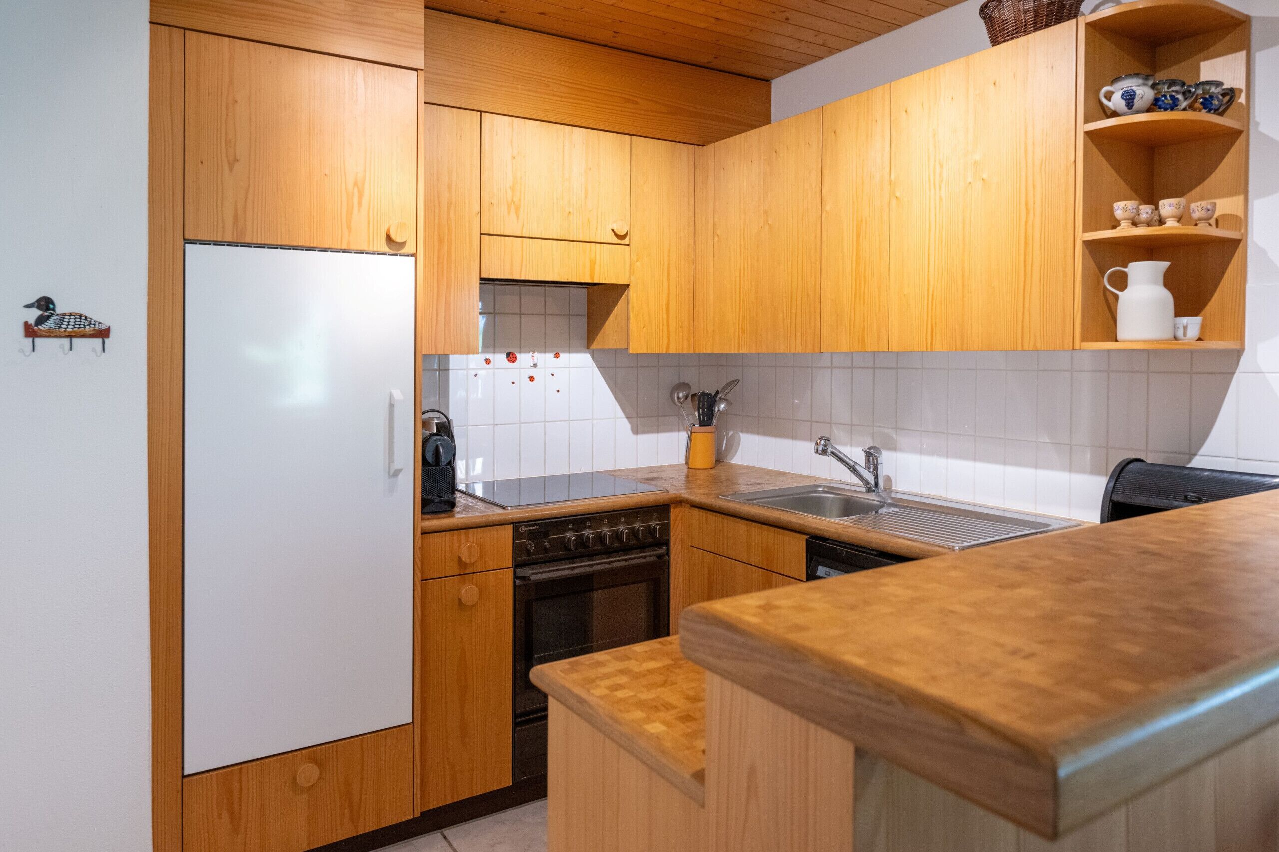 Een keuken met houten kastjes, een koelkast, een fornuis, een spoelbak en een aanrecht.