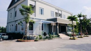 A two-story building with a covered entrance, a car parked in front, and a small tree in the foreground. - The Boone resort (Doi Saket)