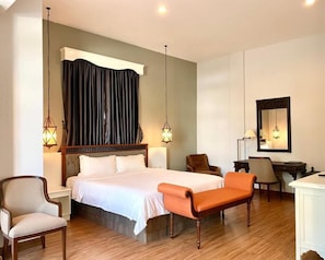 Ein Hotelzimmer mit einem Bett, zwei Sesseln, einem Schreibtisch, einem Spiegel und zwei Pendelleuchten.