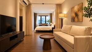 A modern hotel room with a TV, a sofa, a bed, a coffee table, and a painting on the wall. - Amana Living - Nguyen Canh Chan (Ho Chi Minh City)