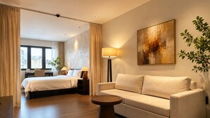 A hotel room with a bed, a sofa, a coffee table, a lamp, and a painting on the wall. - Amana Living - Nguyen Canh Chan (Ho Chi Minh City)